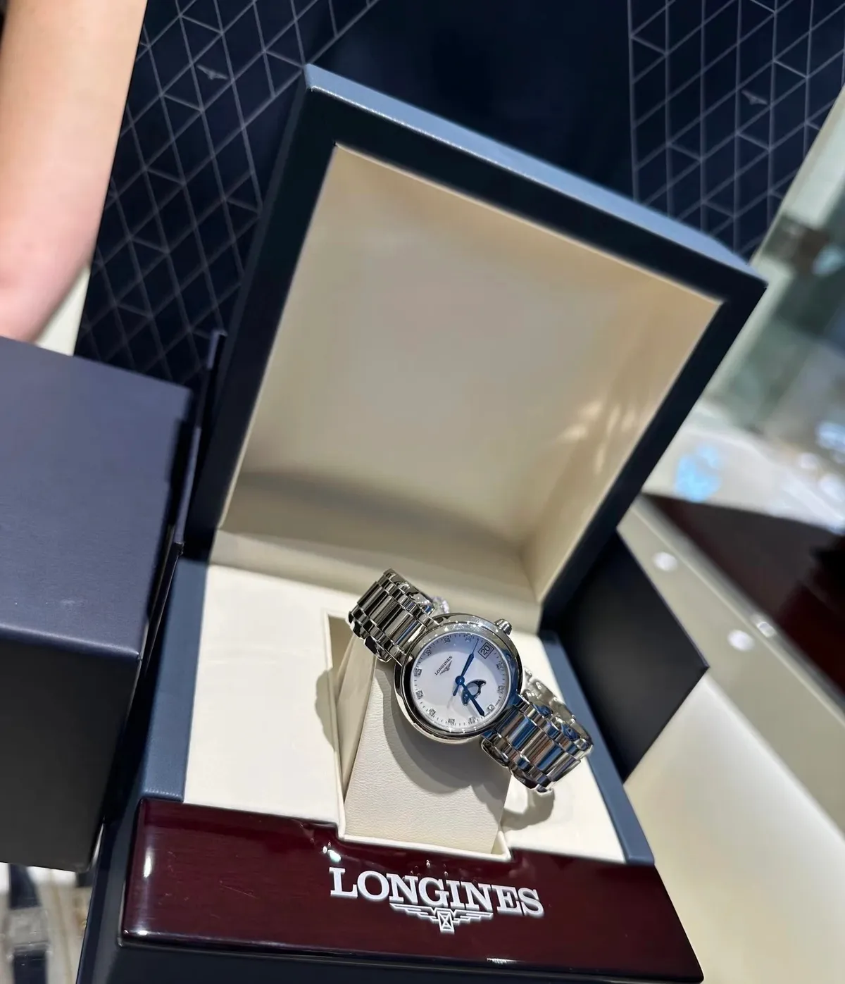 Longines wristwatch with a silver-tone link bracelet, white dial, and blue hands in a presentation box.