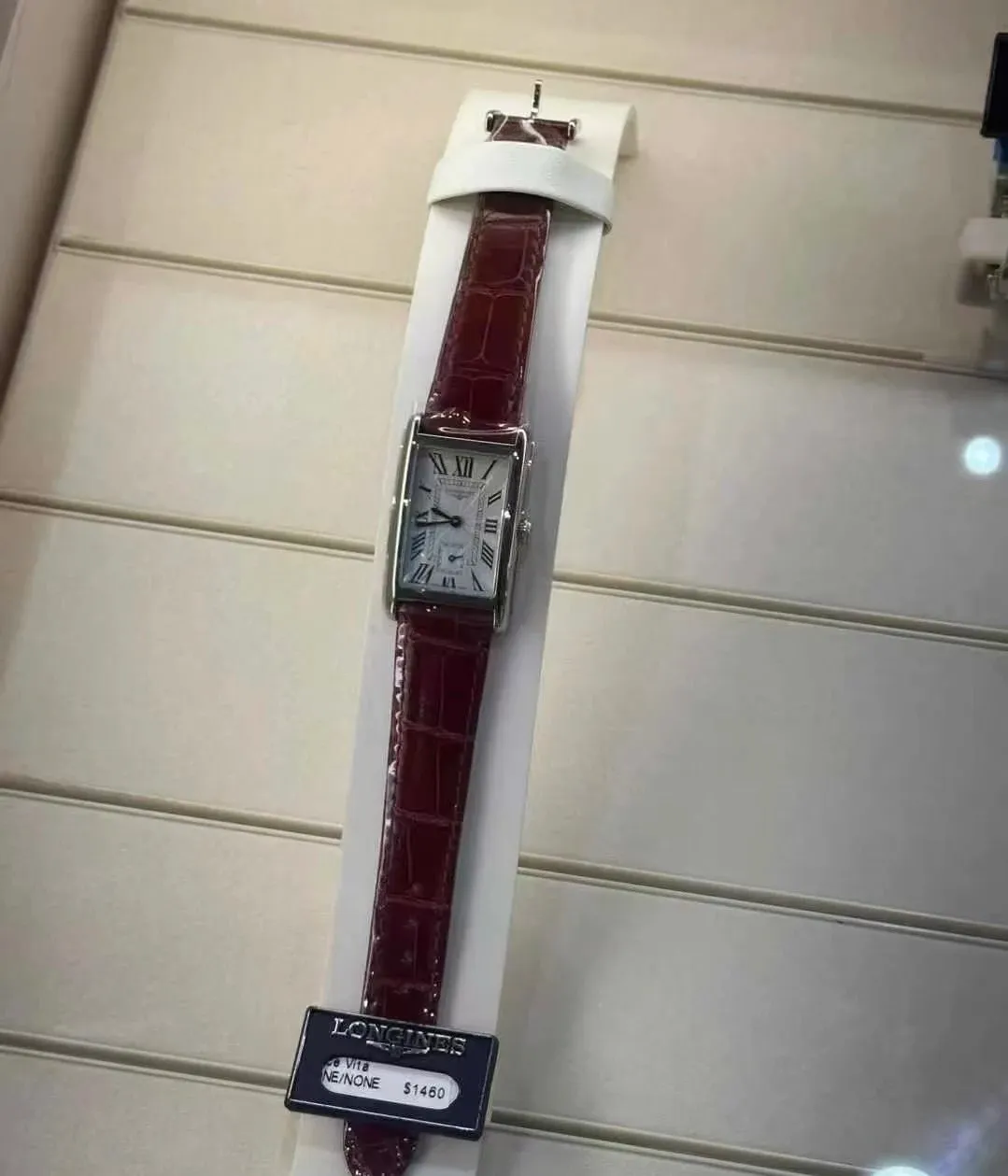 Longines rectangular watch with a burgundy strap, Roman numeral dial, and polished silver case.