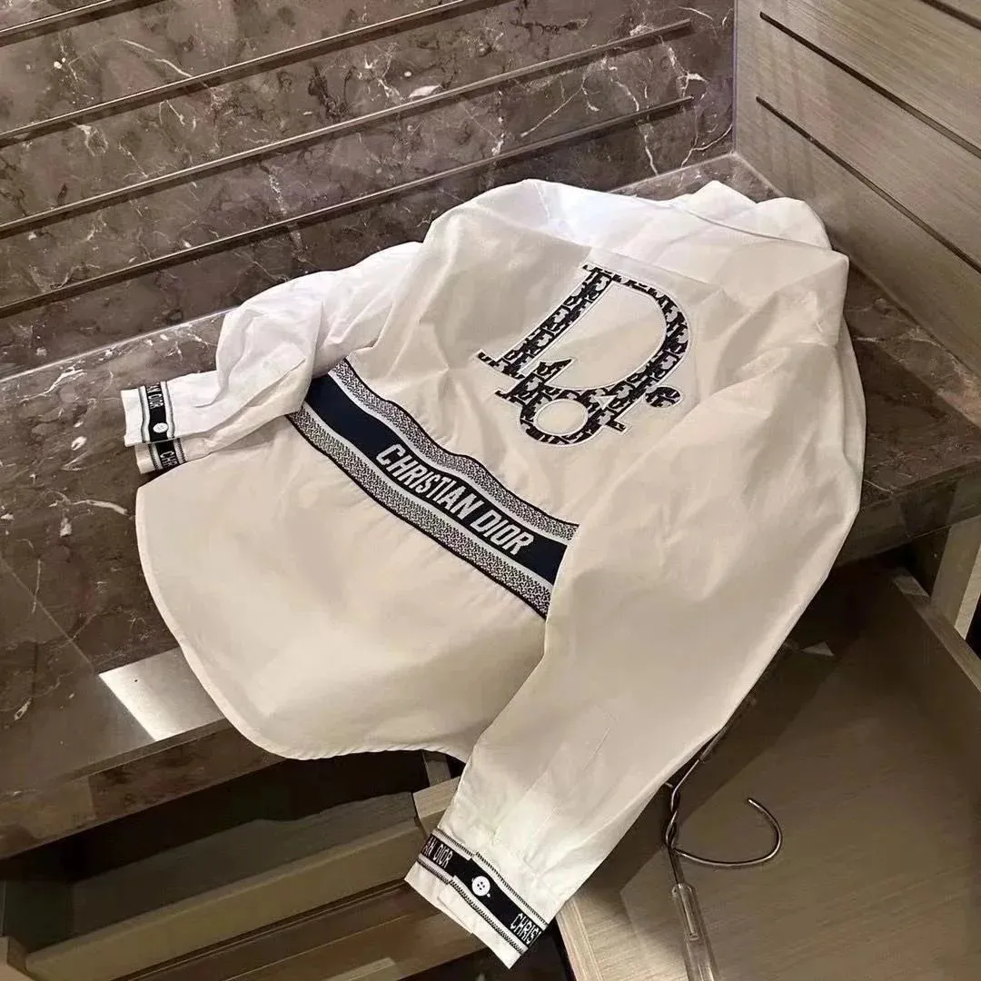 White Dior jacket with CHRISTIAN DIOR chest graphic, striped hem, and cuff logo trim.