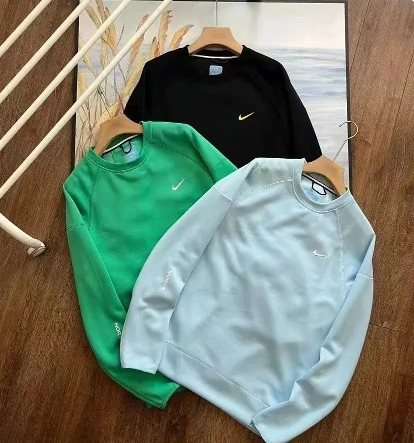 Nike crewneck sweatshirts in black, green, light blue, and white on hangers.