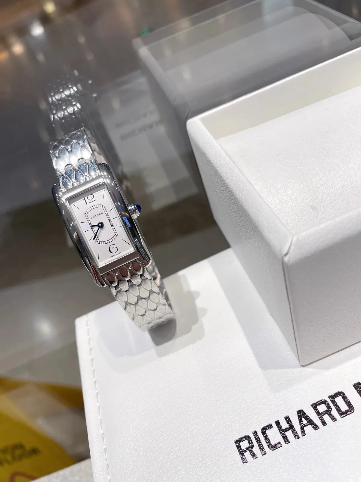Cartier rectangular dial watch with a slim scale-link bracelet and blue crown.