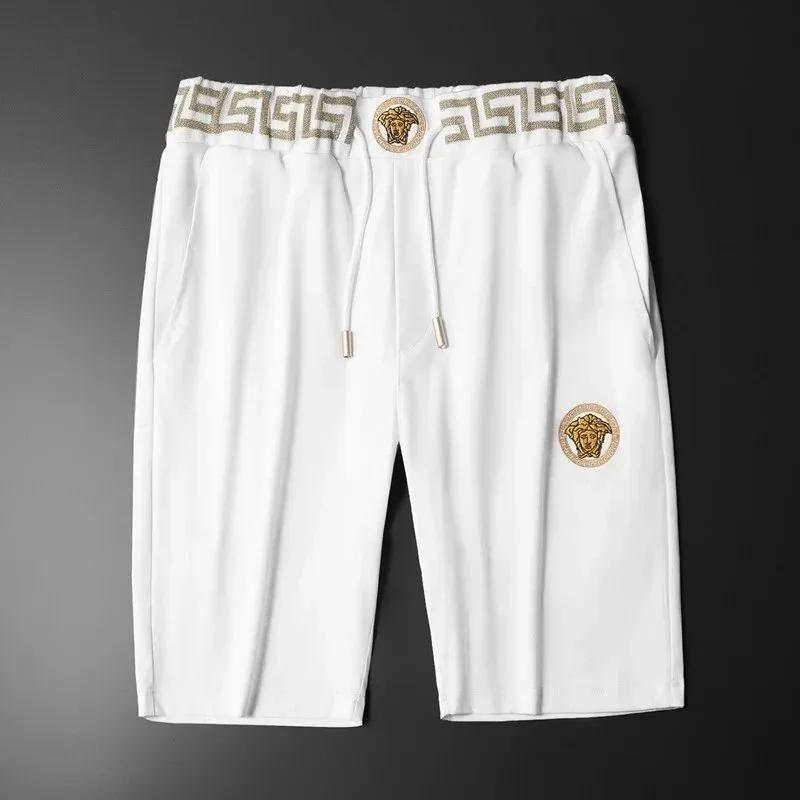 Versace shorts w bieli z wzorem Greek key i naszywką Meduzy na ciemnym tle.