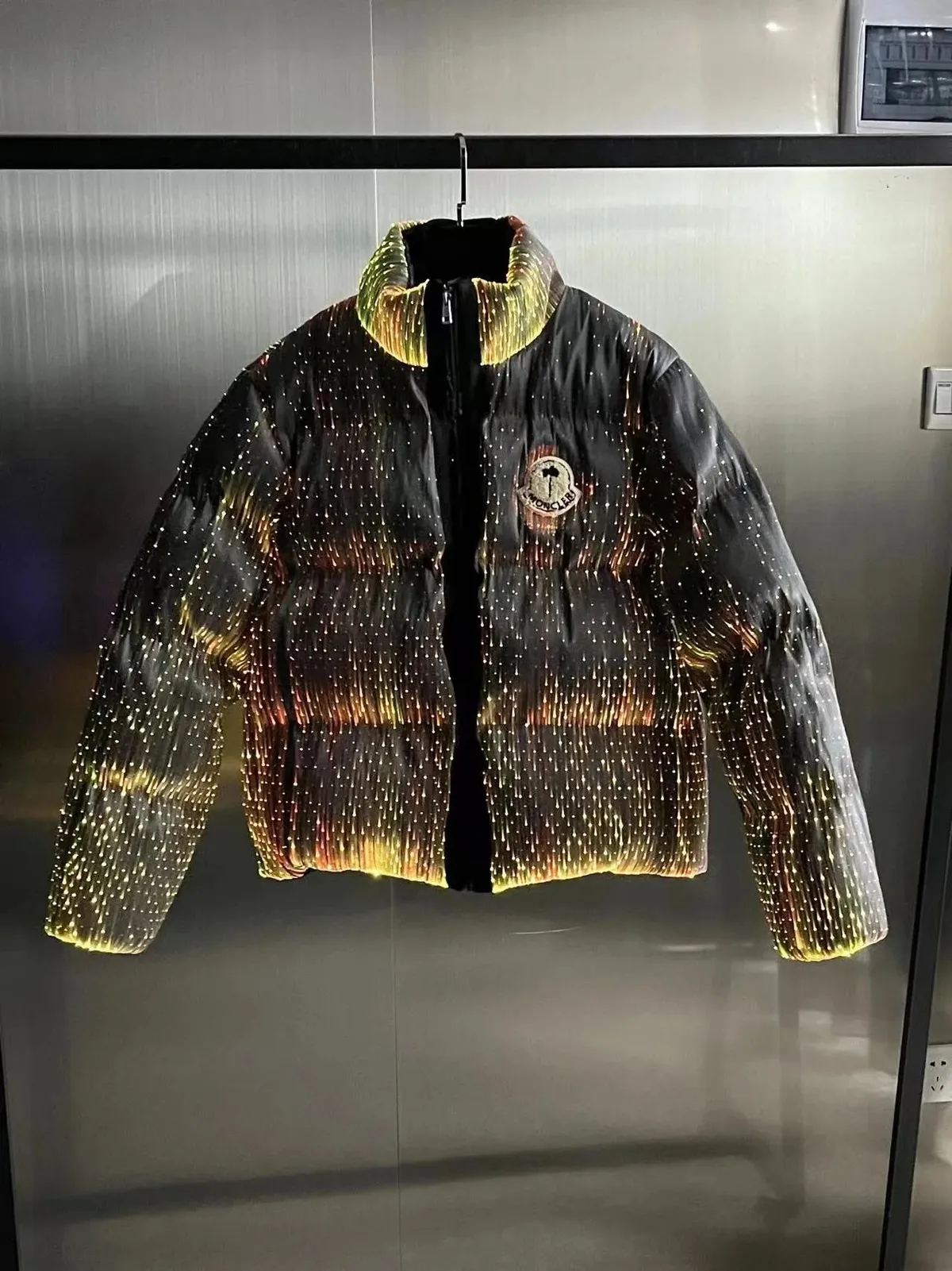 Moncler puffer jacket with a glossy black body and reflective dot pattern on display.