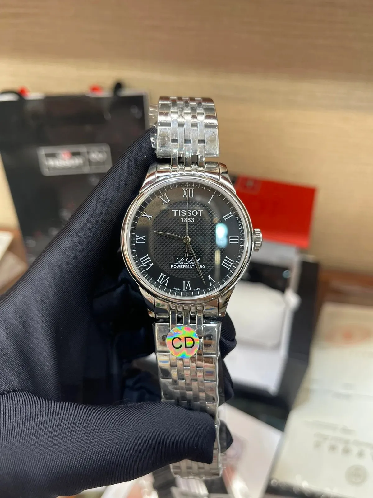 Tissot analog watch with a black dial, Roman numerals, and a silver metal bracelet.