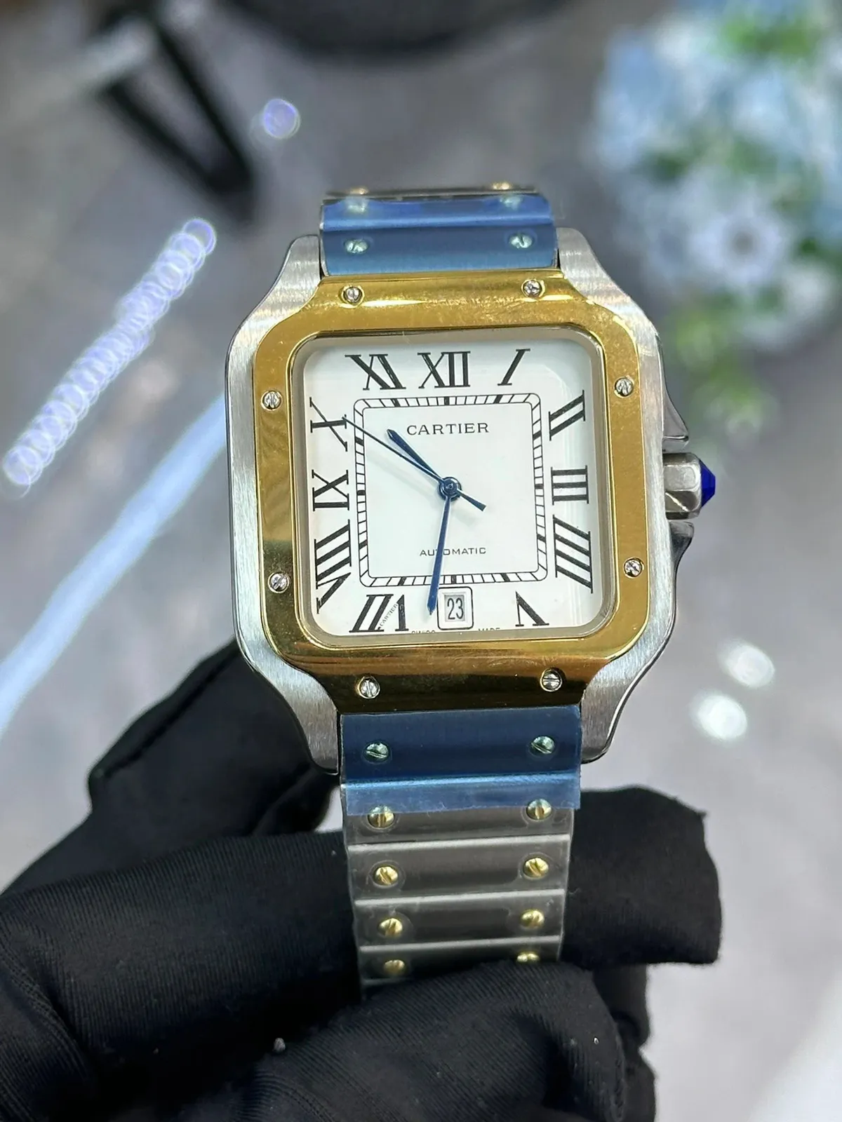Cartier square automatic watch with a two-tone metal bracelet, Roman numerals, and blue hands.