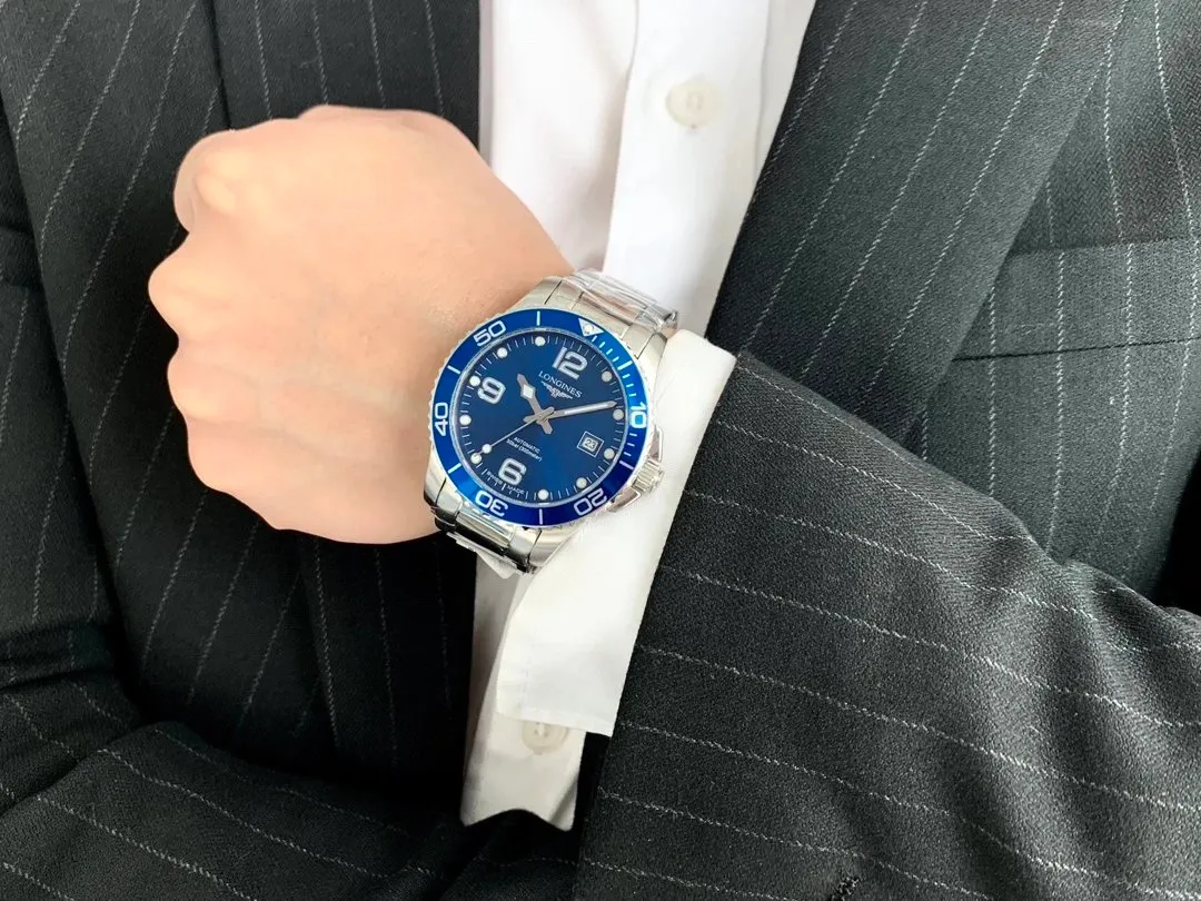 Longines watch with a blue dial and metal bracelet on a suited wrist.